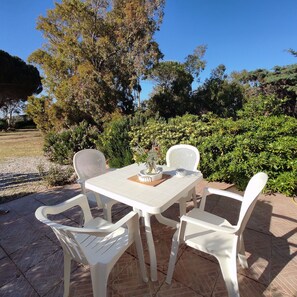 Eine Terrasse mit weißem Tisch und Stühlen, umgeben von Grünpflanzen und Bäumen.