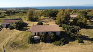 Ein Landhaus mit Ziegeldach, umgeben von Bäumen und Blick auf das Meer.