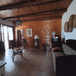 Ein rustikaler Raum mit Holzwänden und -decke, einem Holzstuhl, einem Sofa, einem Tisch, einer Lampe, einem Ventilator und einem Fernseher.