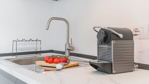 Una cucina moderna con lavello in acciaio inossidabile, macchina per il caffè e tagliere con pomodori.