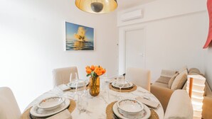 A dining area with a table set for four, a vase with flowers, and a painting of a sunset on the wall.