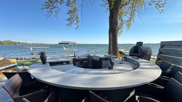 Un espace extérieur circulaire aménagé avec un barbecue, des chaises et une vue sur l’eau.