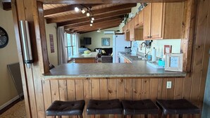 Une cuisine avec des meubles de rangement en bois, un comptoir-bar et trois tabourets.