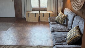 Une pièce avec un canapé, une lampe, une tapisserie murale tissée et une vue sur l’extérieur, visible à travers une porte.