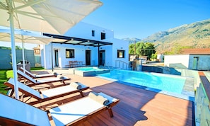 Ein Schwimmbad mit Liegestühlen und Sonnenschirmen, eine überdachte Terrasse und Blick auf Hügel.