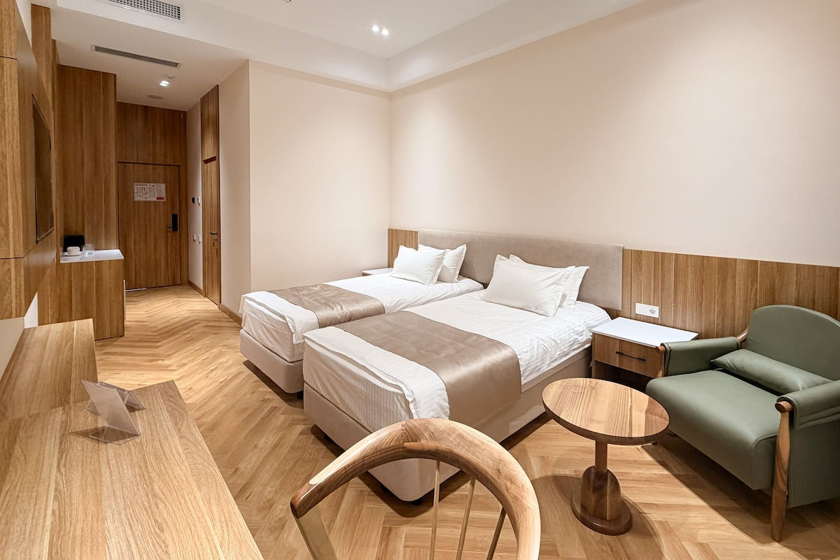A hotel room with two beds, a desk, a chair, and a small table.