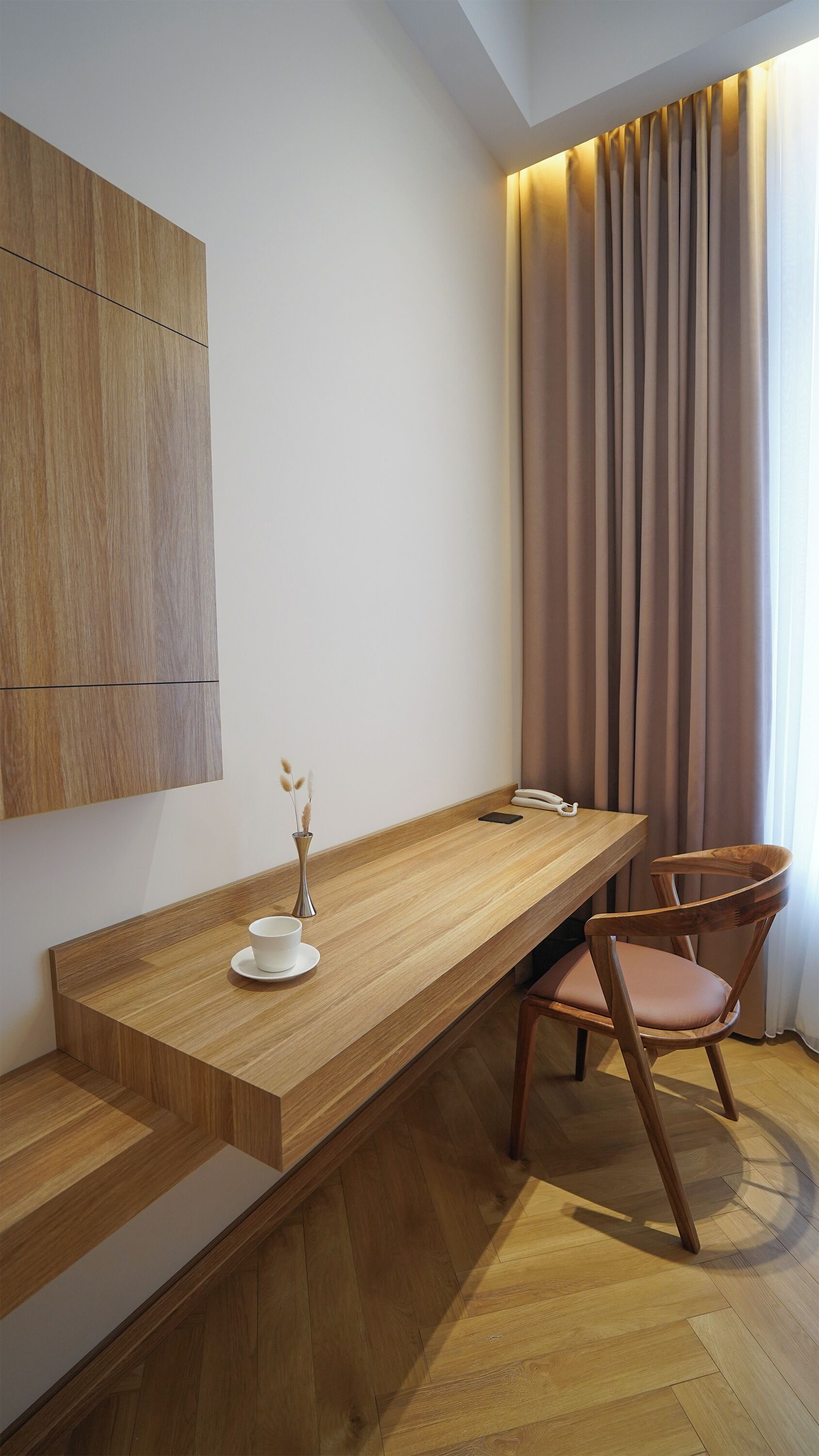 A modern room with a wooden desk, a chair, a vase with dried plants, and a telephone.