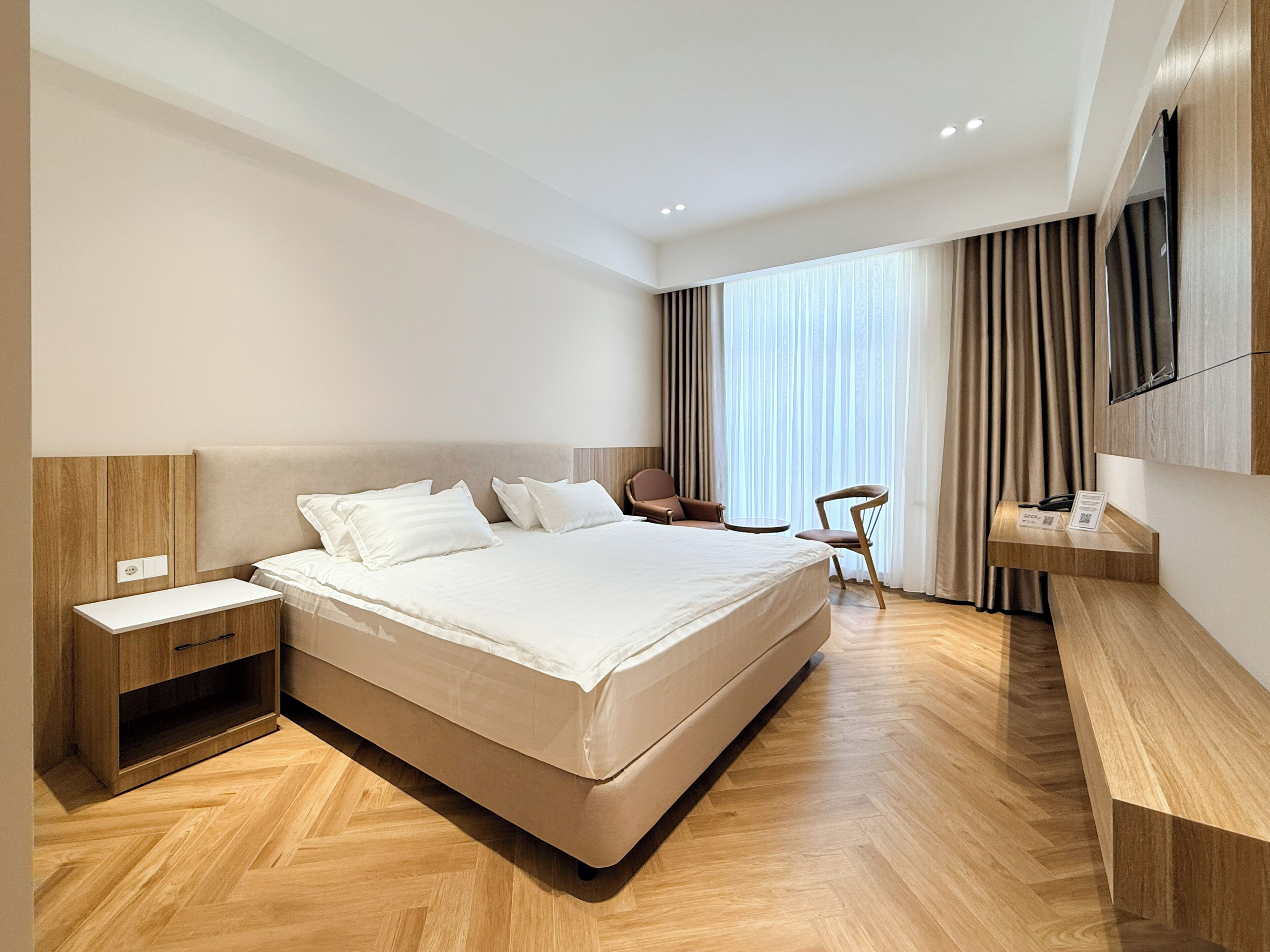 A modern hotel room with a large bed, bedside tables, a desk, and a TV mounted on the wall.