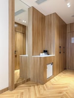 A modern hotel lobby with wooden paneling, a reception desk, and a refrigerator.