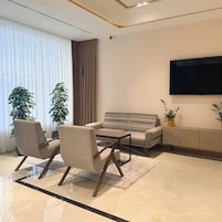 A modern living room with a sofa, two armchairs, a coffee table, a flat-screen TV, and potted plants.