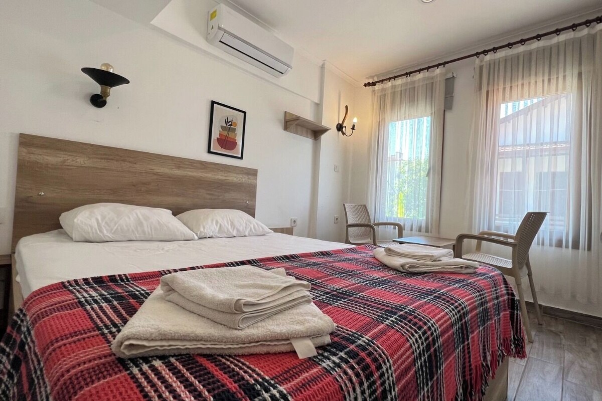 Una habitación de hotel con cama, una silla, un escritorio, aire acondicionado y una ventana con cortinas.