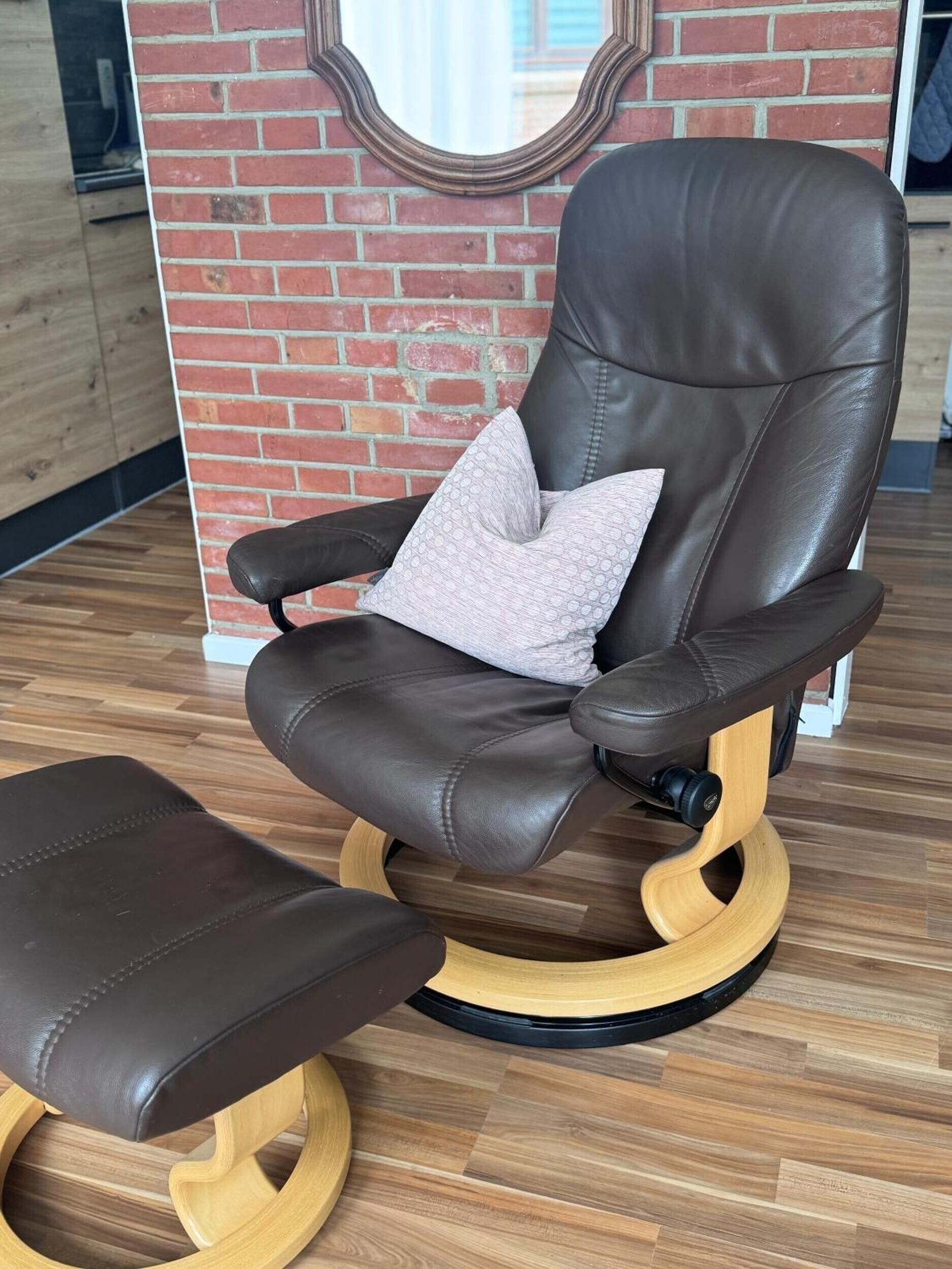 A brown leather chair with a cushion, a matching ottoman, and a wooden base.