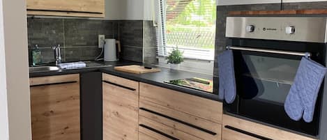 A modern kitchen with wooden cabinets, a built-in oven, and a window with blinds.
