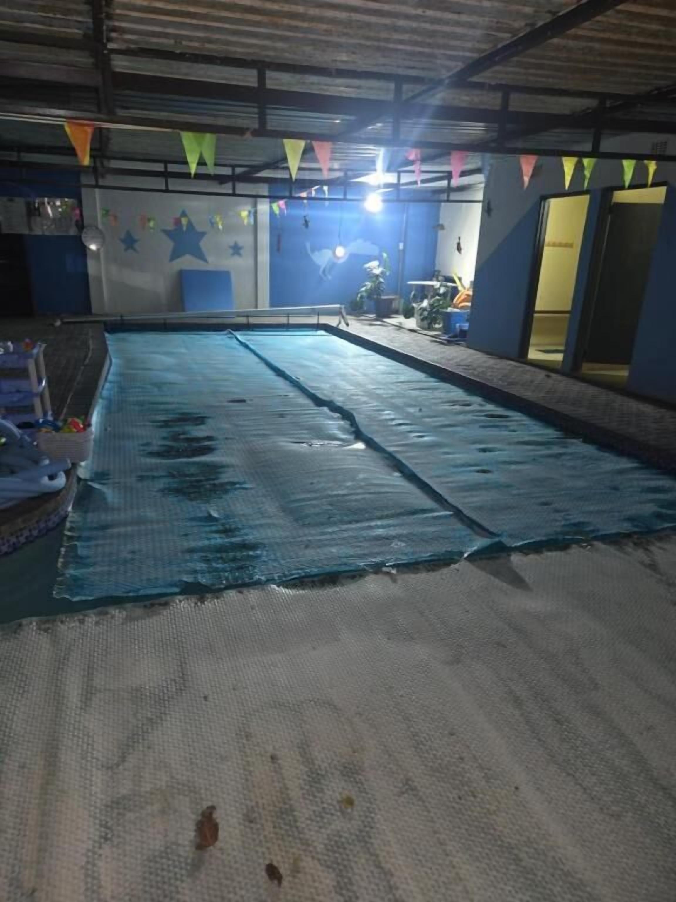 Een binnenzwembad met een blauwe vloer, omringd door muren met sterosdecoraties en een plafond met metalen balken.