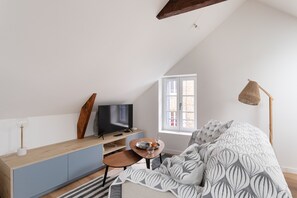 A bedroom with a sloped ceiling, a bed with a patterned blanket, a desk with a television, and a window with a view. - La Petite Maison Bleue - À 400 m de la plage (Dinard)