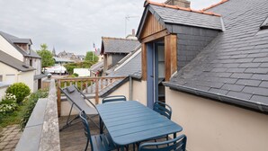 Um imóvel residencial com telhado inclinado, um deck de madeira, uma mesa e cadeiras, e vista para casas vizinhas.