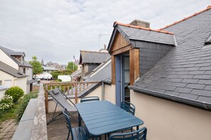 A residential property with a sloped roof, a wooden deck, a table and chairs, and a view of neighboring houses. - La Petite Maison Bleue - À 400 m de la plage (Dinard)