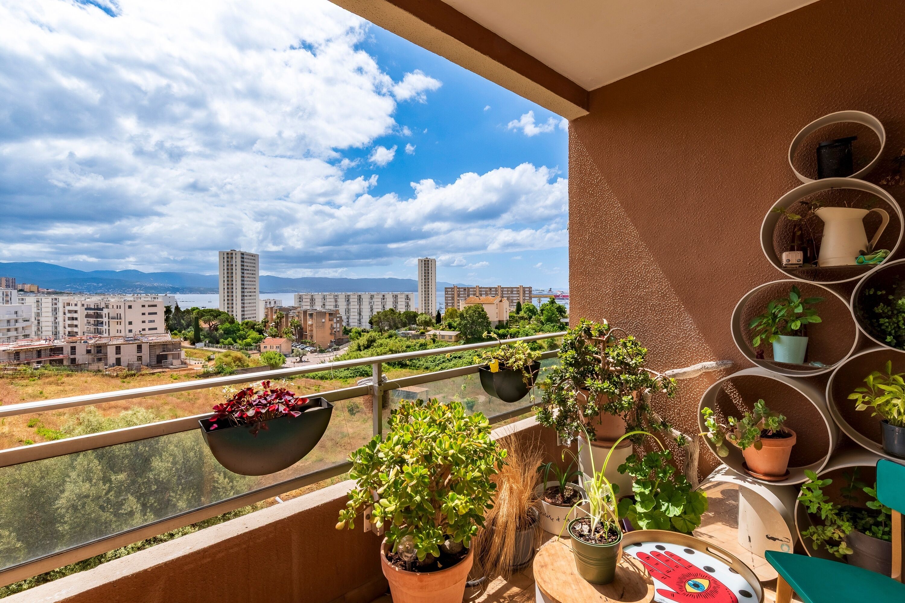 Un balcón con plantas en macetas, vista a un paisaje urbano y cielo despejado.