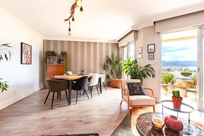 A modern living room with a dining area, large windows, and a view of the city. - Le Lyautey - Charmant appt avec terrasse (Ajaccio)