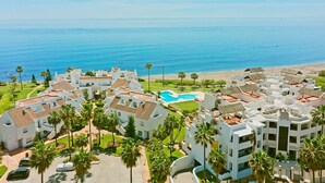 A resort with multiple white buildings, a central swimming pool, and a beach view.