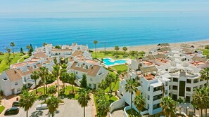 Un resort con varias edificaciones blancas, una piscina central y vistas a la playa.