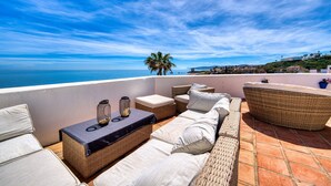 A rooftop terrace with wicker furniture, a table with candles, and a view of the sea.