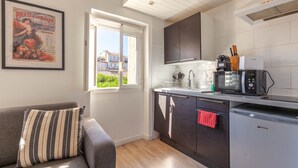 A compact kitchen with a window, a microwave, a dishwasher, and a striped pillow on a sofa. - Le Nid Phocéen - À 700 m du Vieux-Port (Marseille)