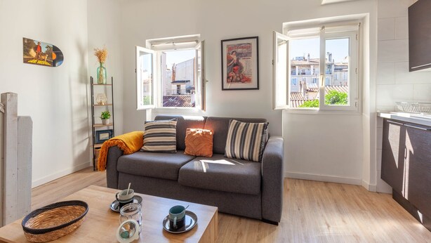 A living room with a sofa, a coffee table, and a window with an open door. - Le Nid Phocéen - À 700 m du Vieux-Port (Marseille)