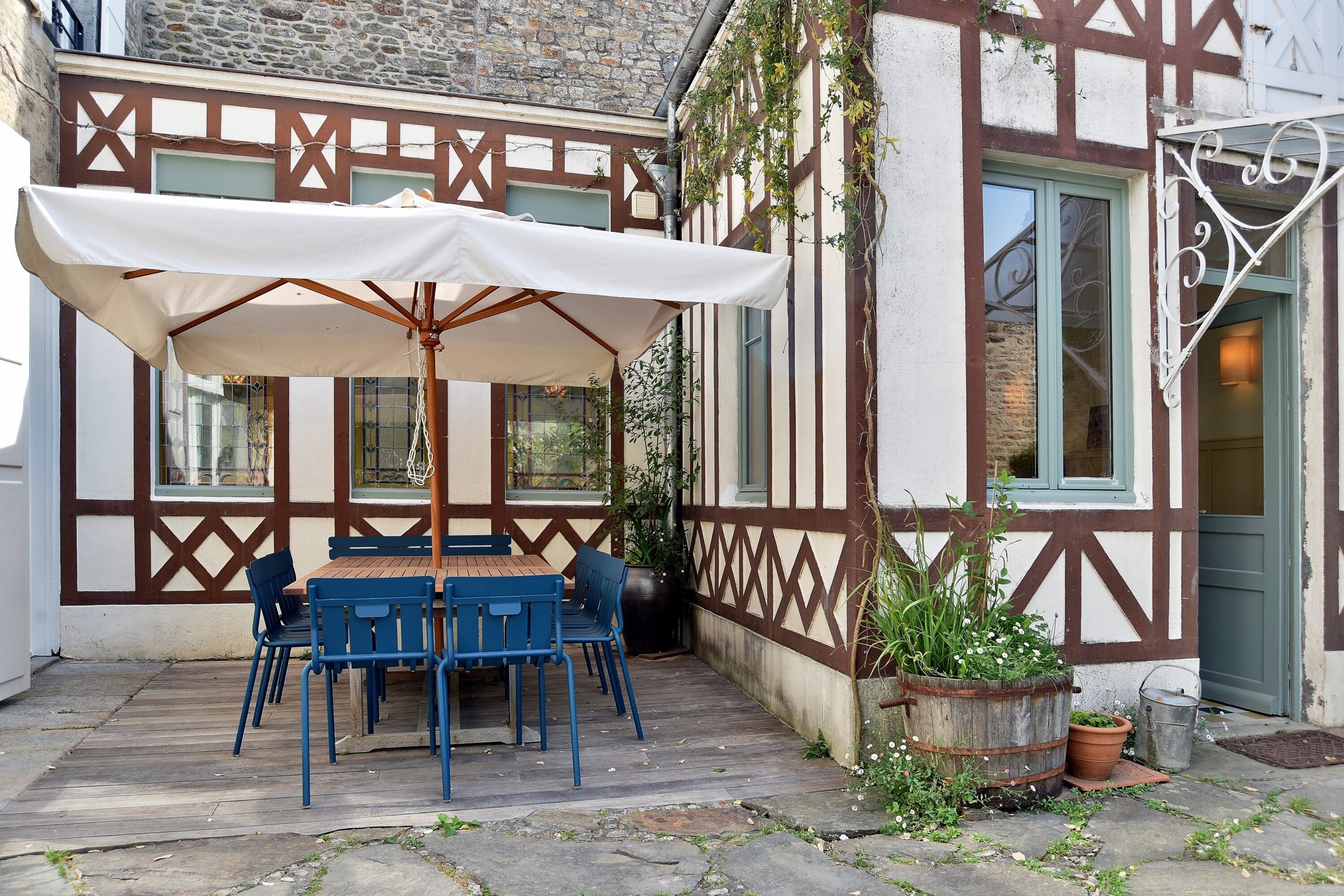 A half-timbered building with a wooden table and blue chairs under a white umbrella.