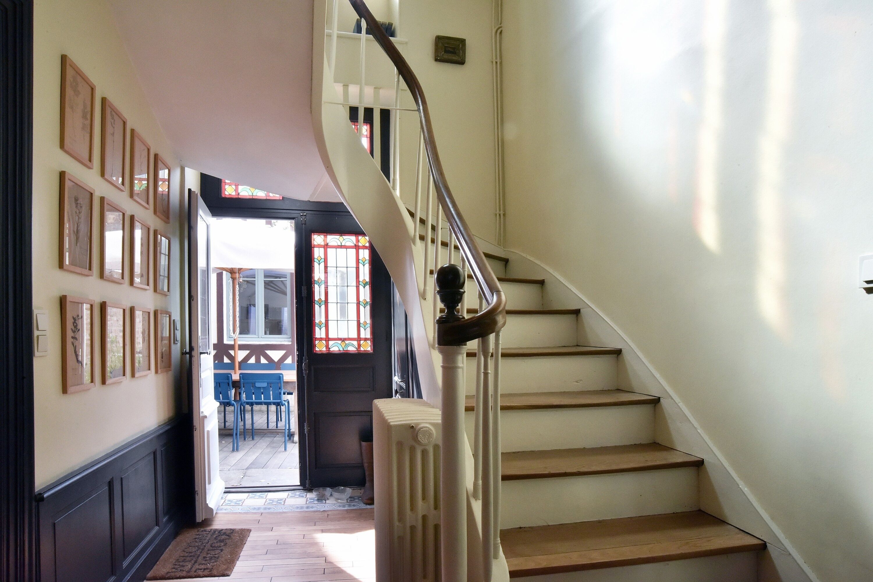 A staircase with a handrail, a radiator, and a door leading to an outdoor area with chairs and a table.