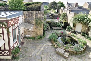 Ein mit Steinplatten belegter Innenhof mit einem kleinen Teich, einer hölzernen Bank und einem Gartenbereich mit verschiedenen Pflanzen.