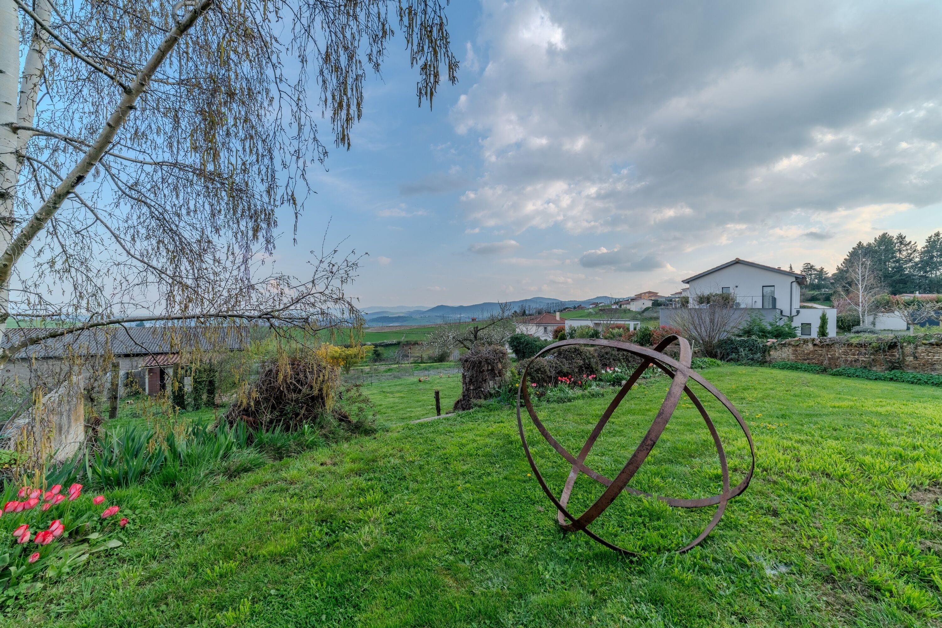 A grassy area with a metal sculpture, a white building, and a view of distant hills.