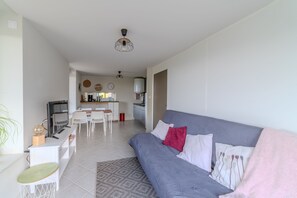 A modern living room with a grey sofa, a TV, and a dining area with chairs and a table. - Deux Pièces, Mille Horizons - Aux environs calmes (Vindry-sur-Turdine)
