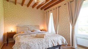 Une chambre à coucher avec un lit, des poutres en bois, un papier peint à motifs et des rideaux.
