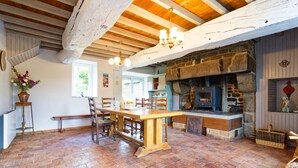 Une cuisine rustique avec une cheminée en pierre, des poutres en bois et un sol carrelé.
