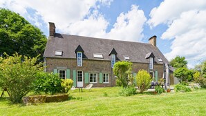 Une maison en pierre avec un toit en pente, de nombreuses fenêtres et un jardin bien entretenu.