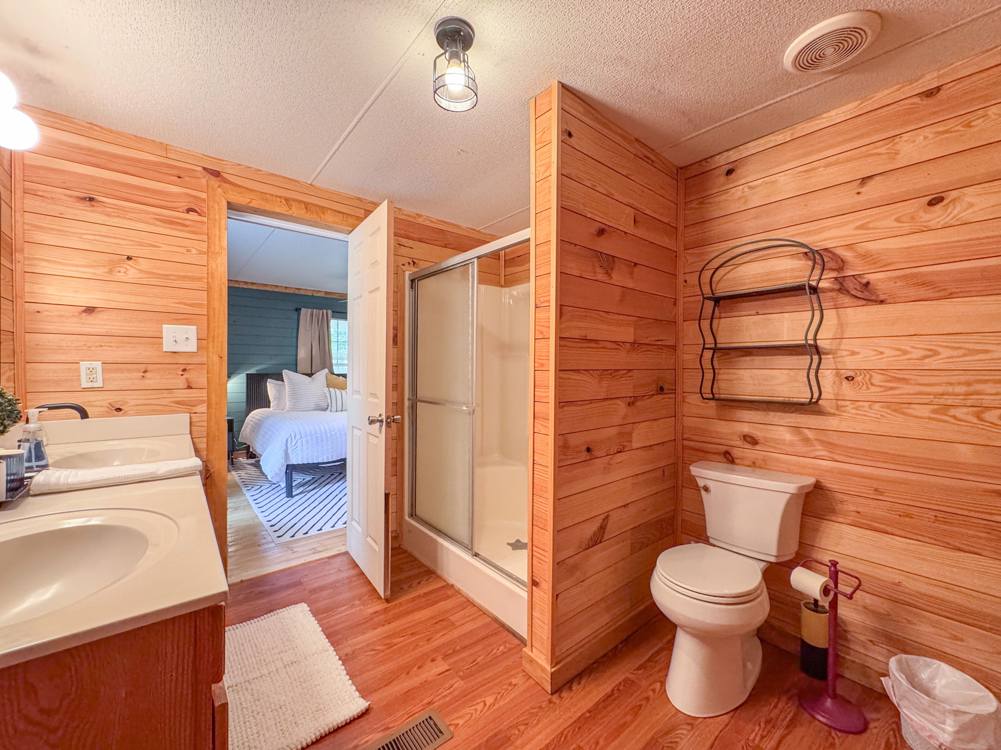 A wooden-paneled bathroom with a shower, toilet, and sink.