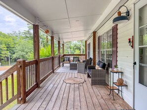 A covered porch with wooden railings, wicker furniture, and a view of a lake.