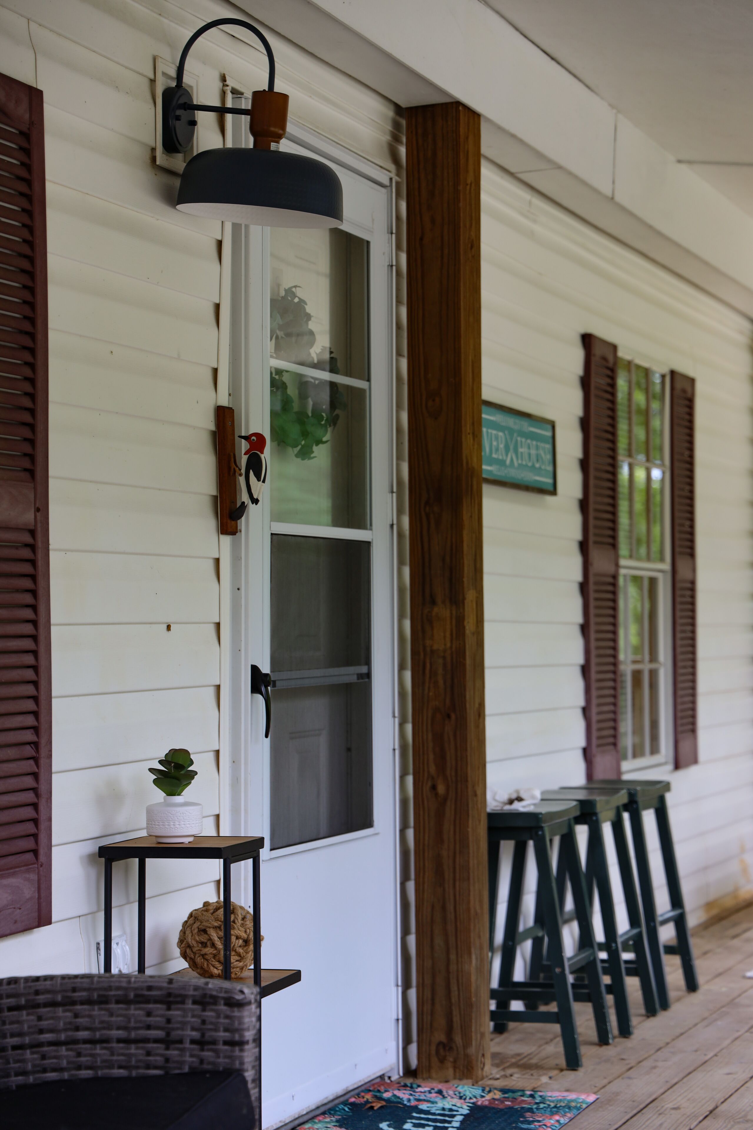A porch with a white door, wooden shutters, a hanging light fixture, a small table with a plant, and a sign that reads 'VERXHOUSE'.