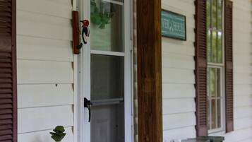 A porch with a white door, wooden shutters, a hanging light fixture, a small table with a plant, and a sign that reads 'VERXHOUSE'.