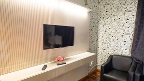 Un soggiorno moderno con una televisione a schermo piatto montata su una parete bianca, pavimento in legno e un divano in pelle nera.