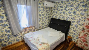 Una stanza con un letto, carta da parati floreale, pavimento in legno, una finestra con tende e un condizionatore d'aria.