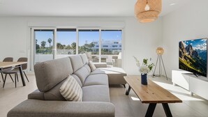 A modern living room with a sofa, dining table, and a TV on a white wall. - 3024 Bright Apartment with Terrace and Pool (Bel-Air)