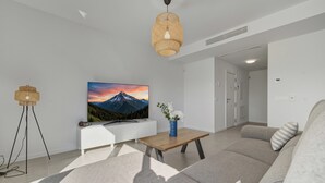 A modern living room with a sofa, a coffee table, a TV, and a wall-mounted lamp. - 3024 Bright Apartment with Terrace and Pool (Bel-Air)