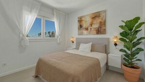 A bedroom with a bed, a window with curtains, a wall-mounted painting, bedside lamps, and a potted plant. - 3024 Bright Apartment with Terrace and Pool (Bel-Air)