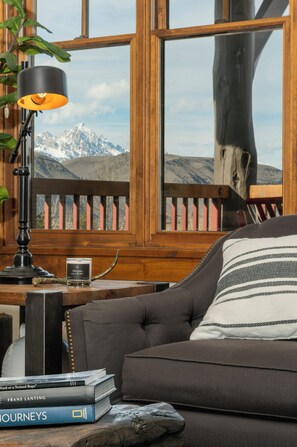 Ein gemütliches Zimmer mit Bergblick, einer Lampe, Büchern und einer Kerze auf einem Holztisch.