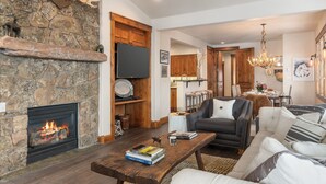 Ein Kamin aus Stein, ein Holzesstisch, eine Couch und eine Deckenleuchte in einem Wohnzimmer.
