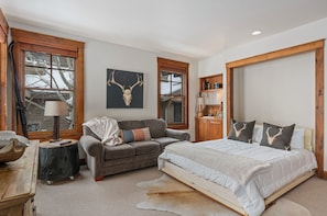 A bedroom with a bed, a sofa, a lamp, a wooden cabinet, and a wall-mounted artwork. - Outpost: Grand View 363S - Air Conditioning! (Jackson)