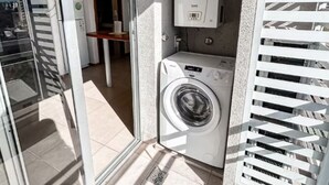A balcony with a washing machine, a water heater, and a glass door leading to an interior room. - Cómodo dpto. en Salta para dos personas (Salta)