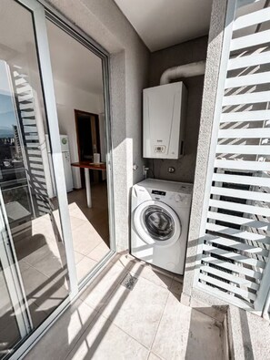 Ein Balkon mit Waschmaschine, Boiler und Glastür zu einem Innenraum.